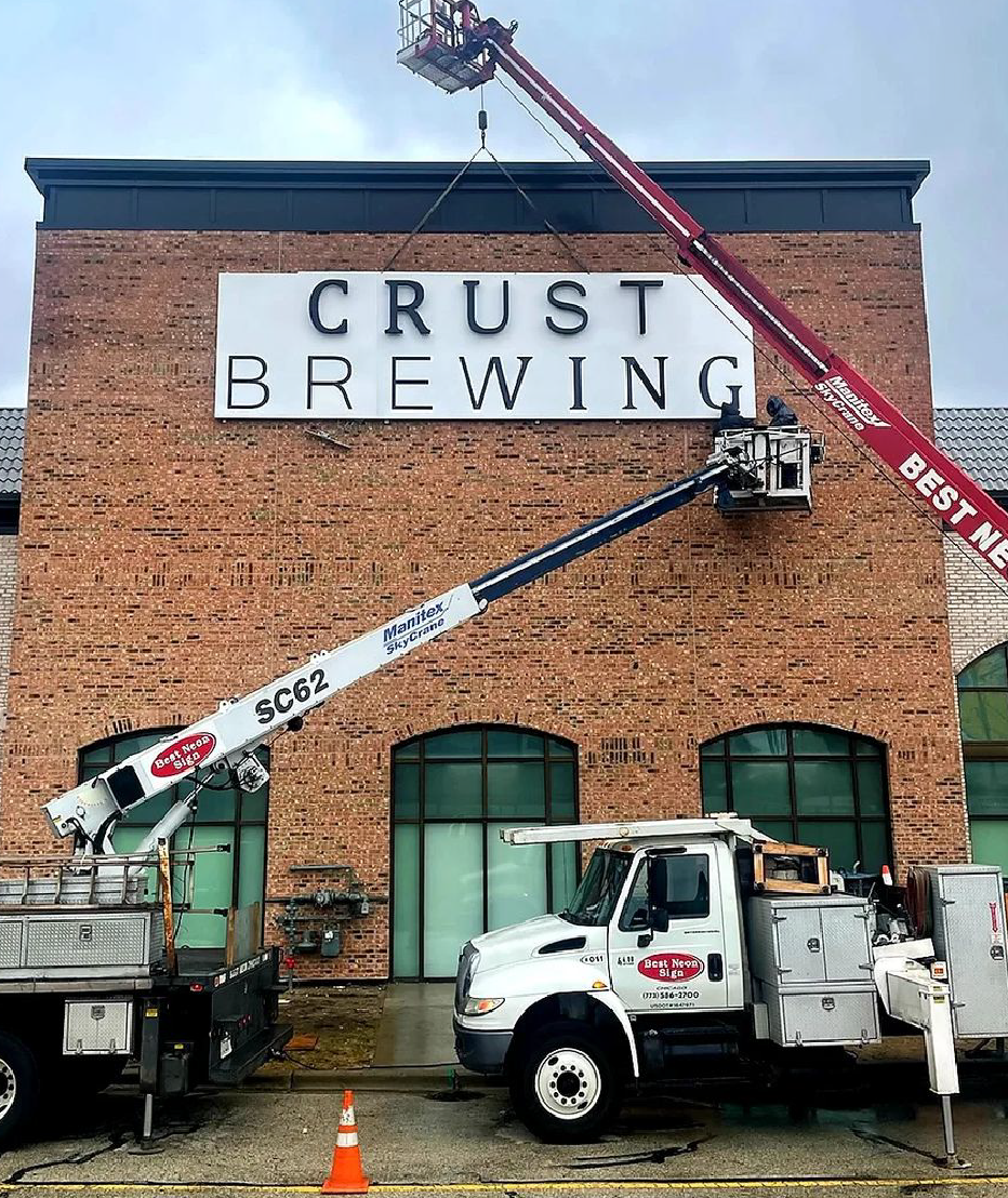 Building letters going up on a brick facade with two boom trucks