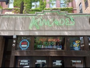 Kincade's storefront with green neon script sign and neon window signs